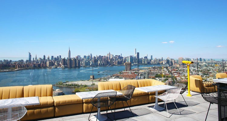 Bright yellow sofas with marble tables and black and white wire chairs on a sunny patio with a cityscape view in the background